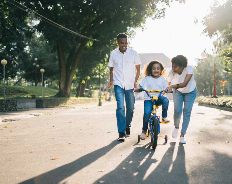 man standing beside his wife teaching their child how to ride a bike